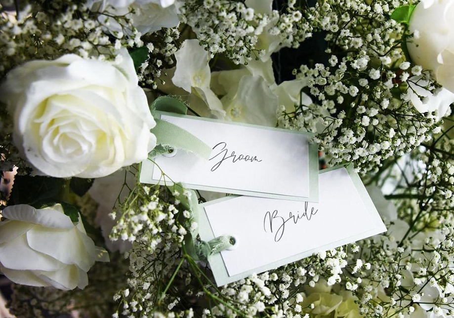 Sage coloured bride and groom place notes on a background of white roses and babies breath